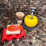 תמונת מוצר של סט צבעוני ושמח- מגש אובלי סבוניה תלתלית וכוס כדורי בעיצוב לא שמרני, מונח באמבטיה, עם סבון טבעי ומברשת גילוח