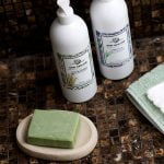 סבוניה אובלית בדוגמת אבן כורכר במקלחת יוקרתית, עם סבון ירוק מונח עליה